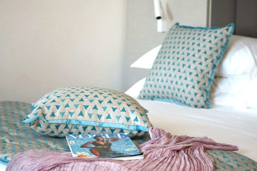 A bed with patterned pillows, a magazine, and a pink blanket.