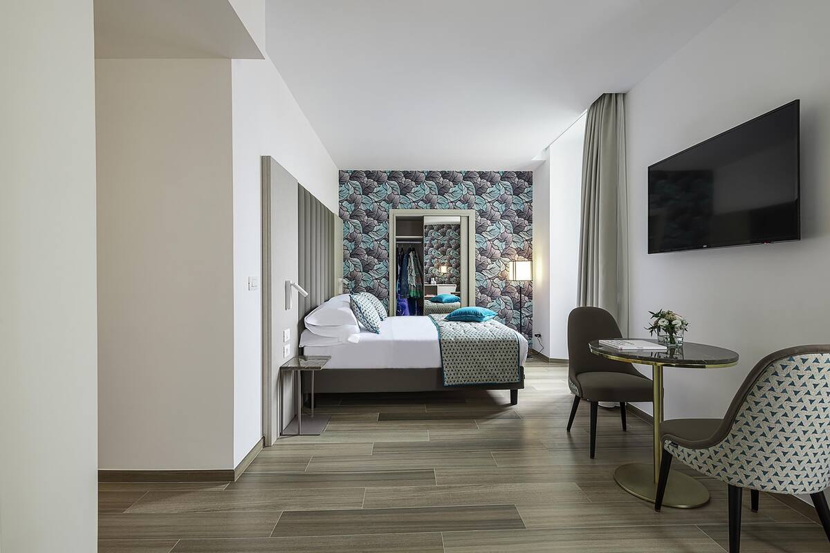 Een hotelkamer met een bed, een televisie, een klein tafeltje met een vaas en een stoel.