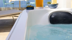 Een bubbelbad met een drankje en een schaal olijven, een tafel met stoelen en uitzicht op zee.