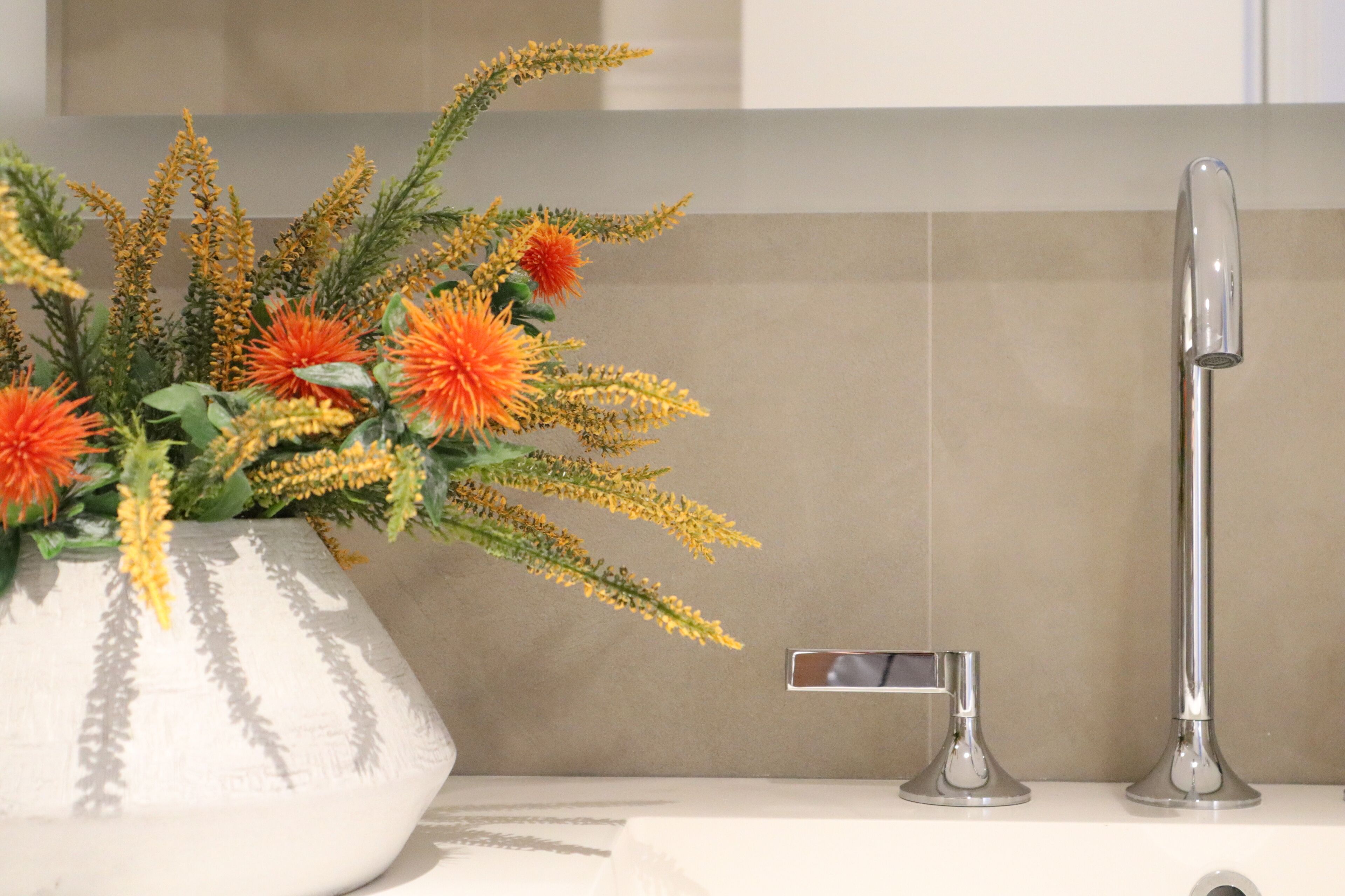 A bathroom with a white sink, a modern faucet, and a decorative vase with orange flowers.