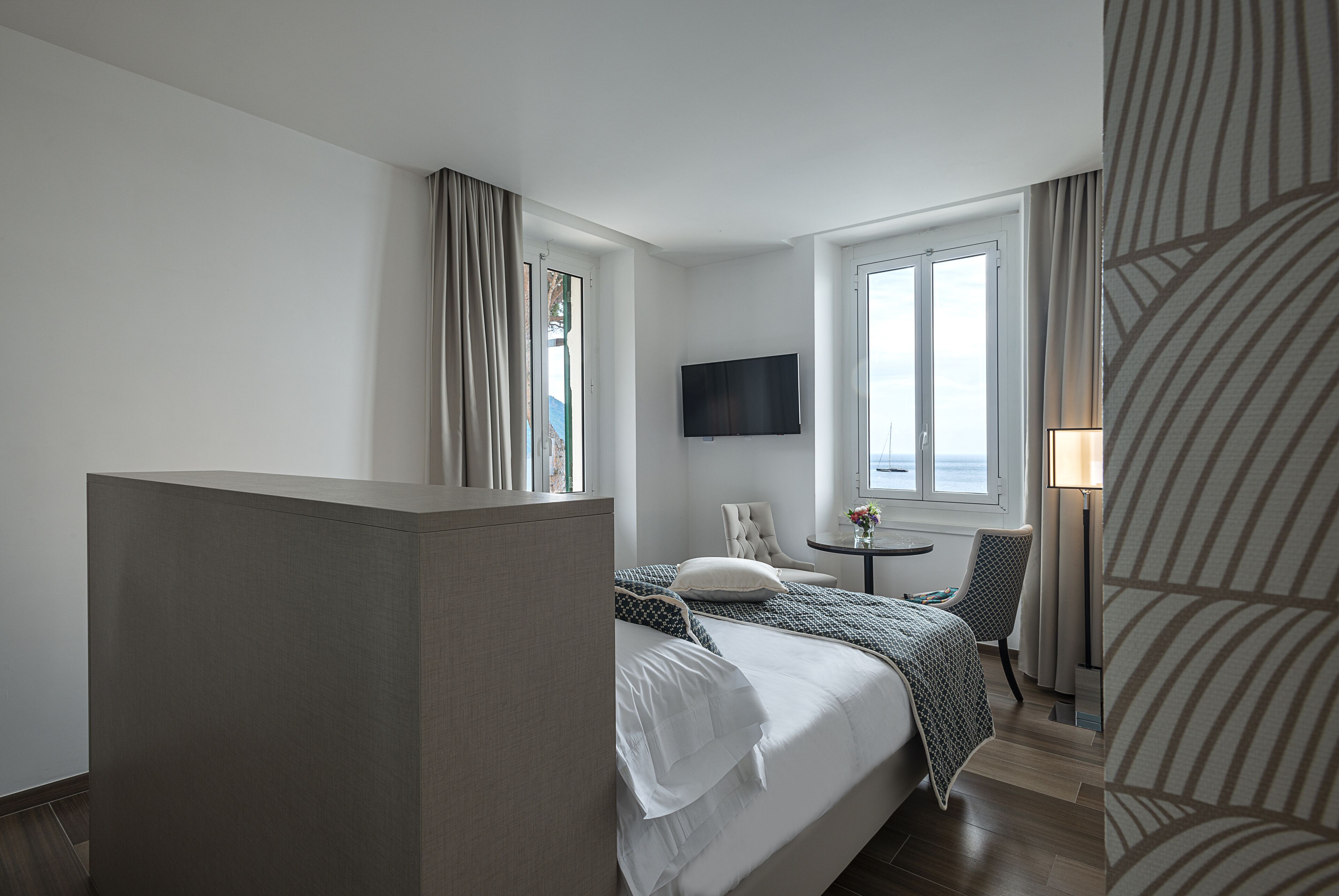 A hotel room with a bed, a chair, a TV, and a window with curtains.