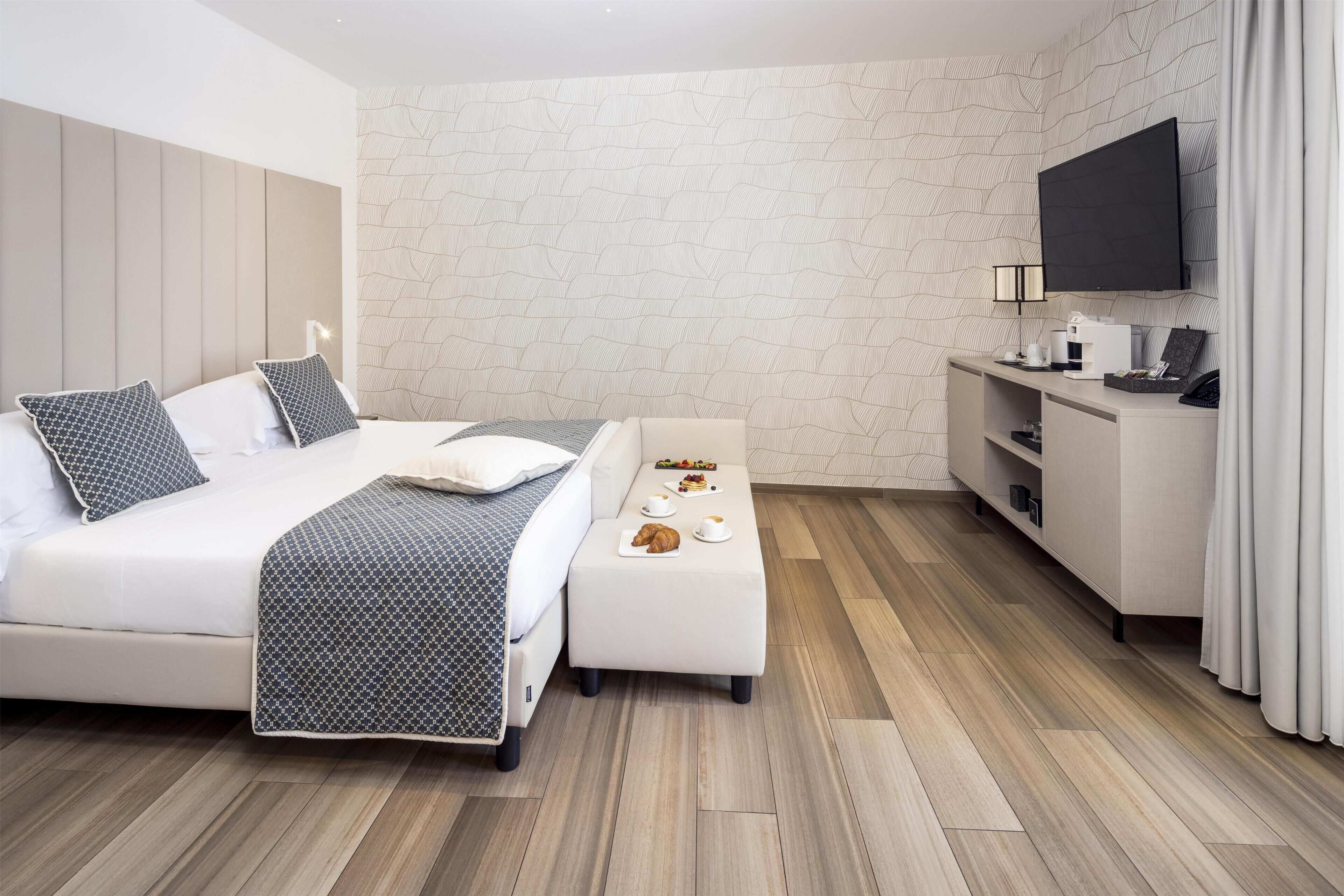 Ein modernes Hotelzimmer mit Bett, einer kleinen Sitzecke, einem Schreibtisch und einem Fernseher.