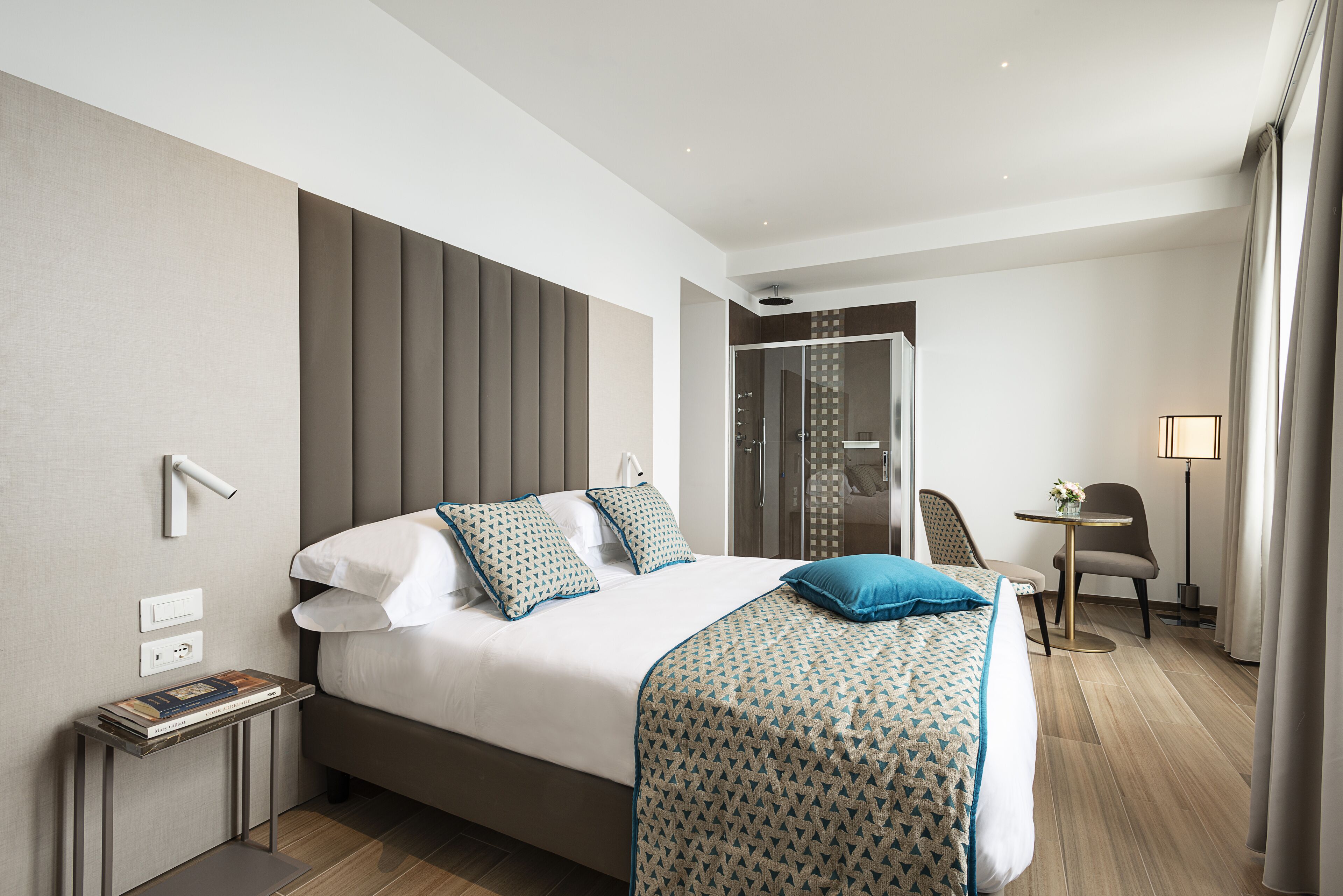 Una habitación de hotel moderna con una cama grande, mesitas de noche, un escritorio pequeño y zona de ducha.