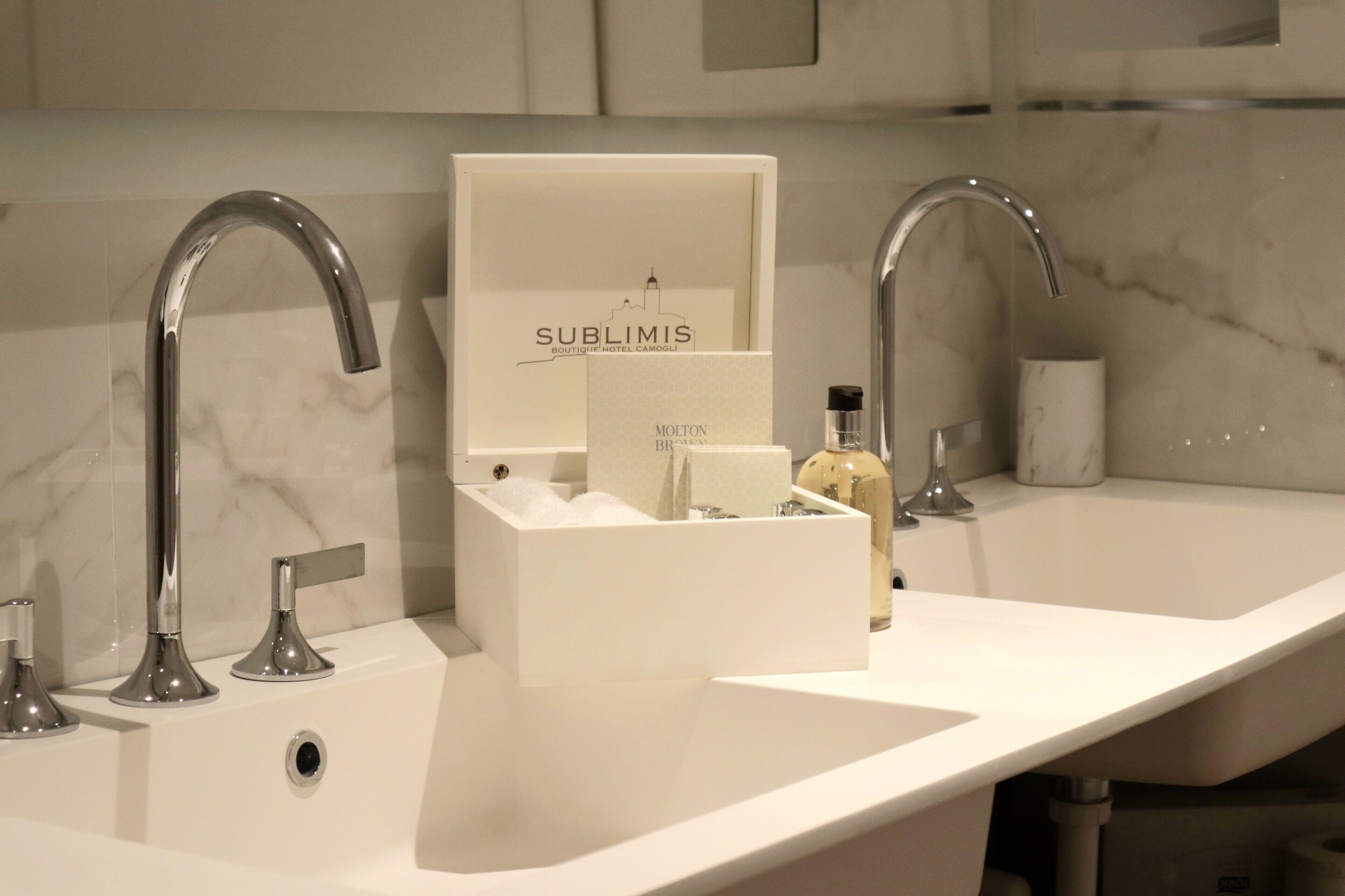 Ein modernes Badezimmer mit zwei Waschbecken, einem Spiegel und einer mit 'Sublimis' beschrifteten Schachtel mit Toilettenartikeln.