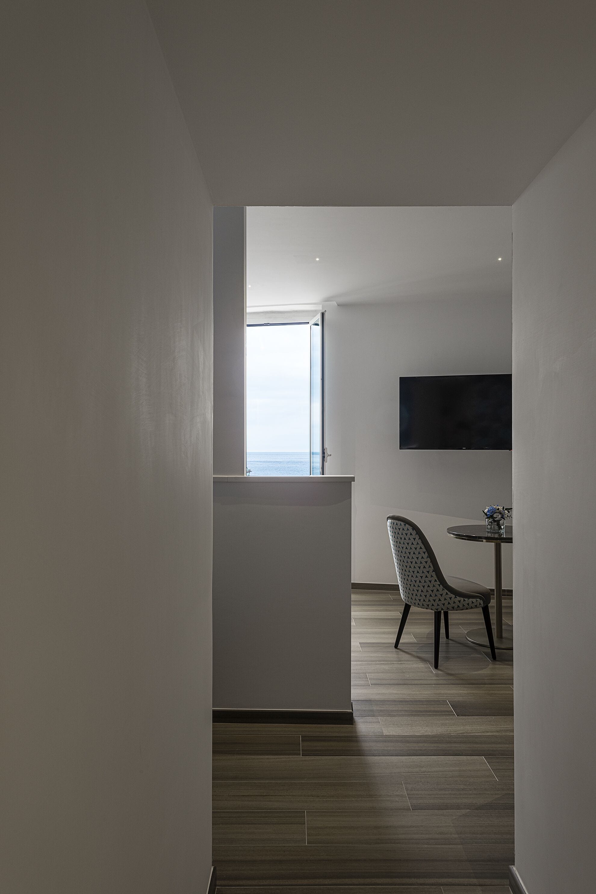 A modern, minimalist room with a large window, a flat-screen TV, and a dining area with a chair and table.