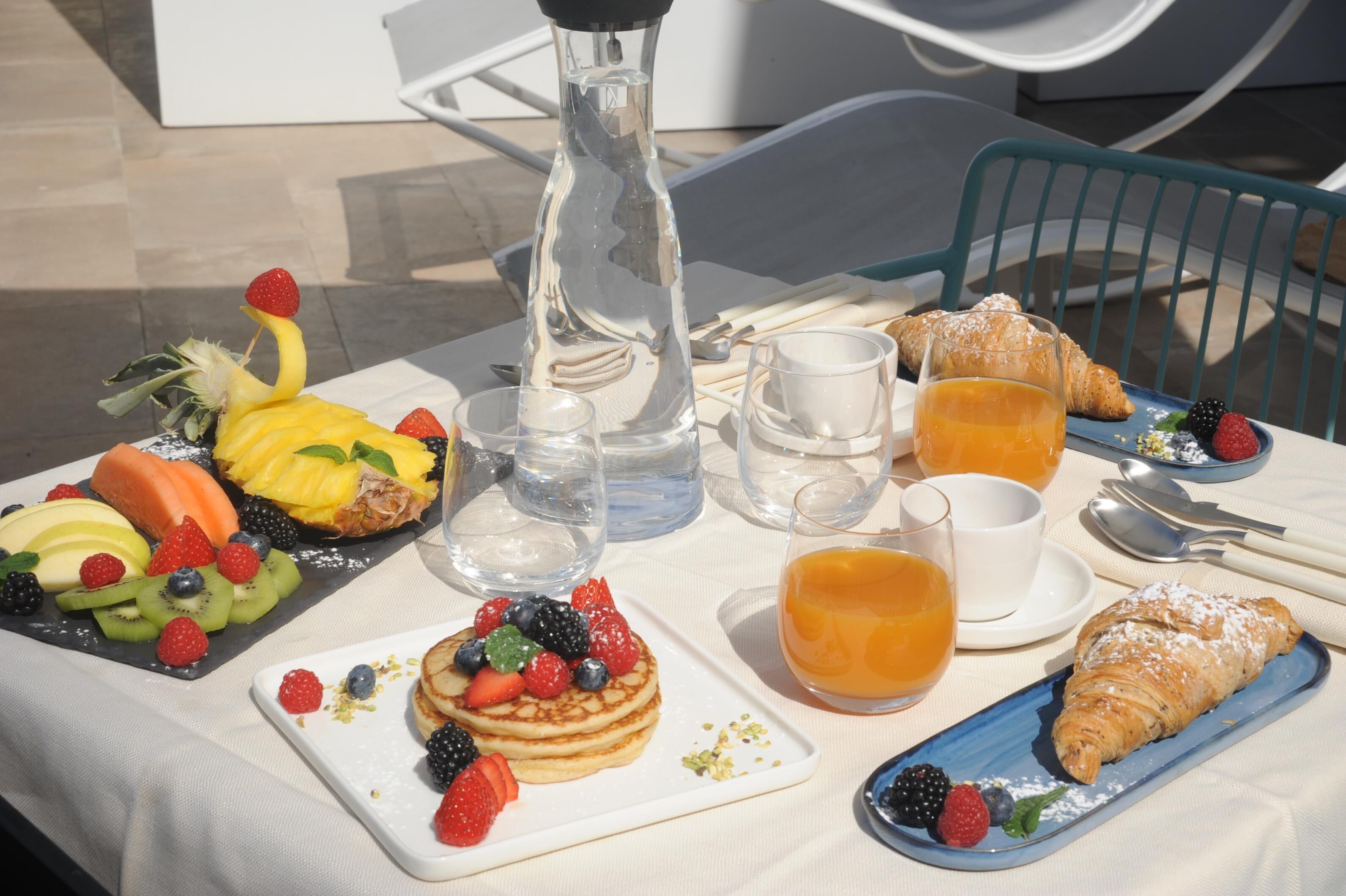 Ein Esstisch mit Pfannkuchen, Croissants, Obst und Saft.