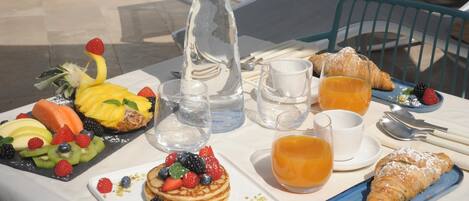 Ein Esstisch mit Pfannkuchen, Croissants, Obst und Saft.