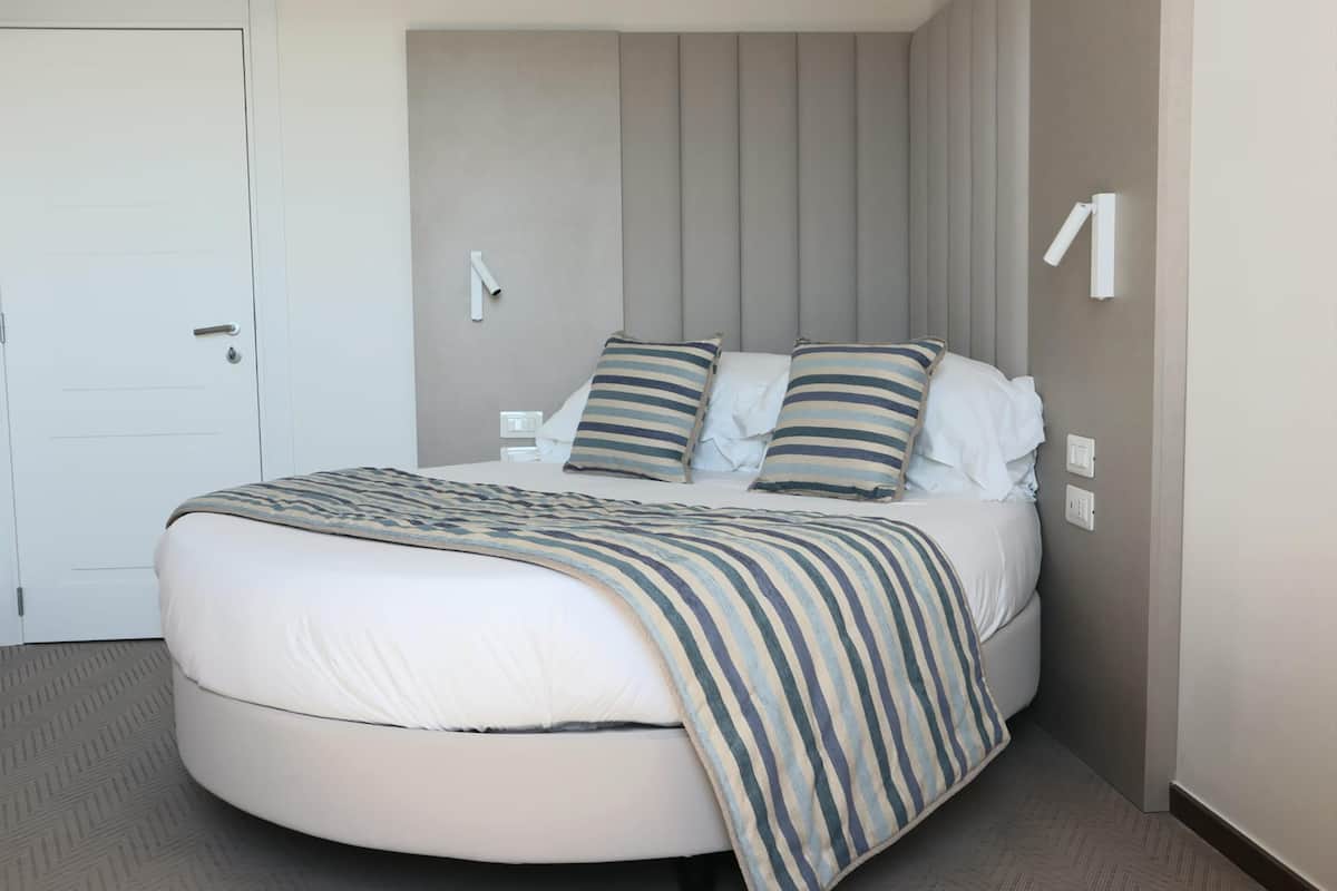 Een rond bed met een gestreept dekbed, een nachtkastje en een wandlamp.