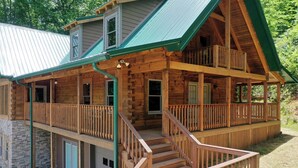 A two-story log cabin with a balcony on the upper floor, a stone foundation, and a covered front porch. - This 5 bedroom 5 bath log cabin with spectacular views, secluded, & Hot-tub (Townsend)