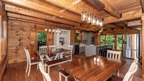 A wooden cabin interior with a dining area, kitchen, and large windows. - This 5 bedroom 5 bath log cabin with spectacular views, secluded, & Hot-tub (Townsend)