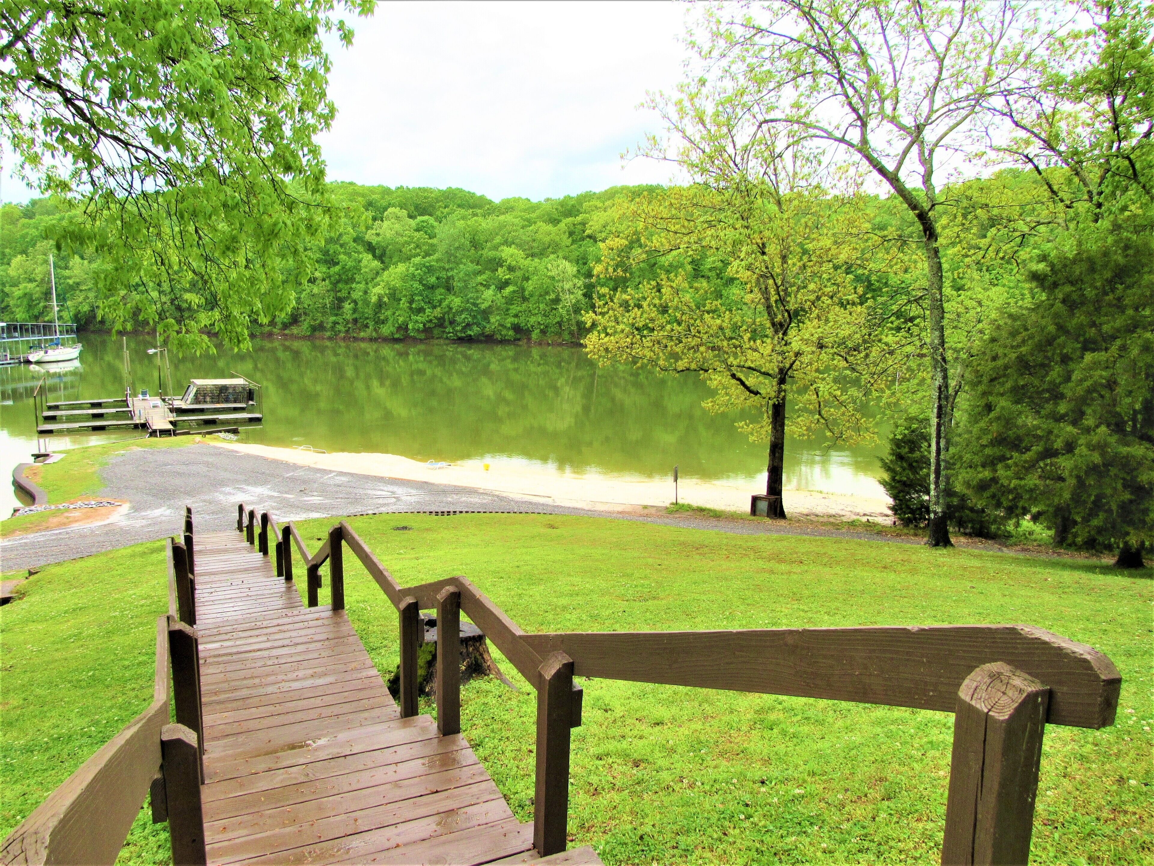 A wooden staircase leading to a dock by a lake surrounded by lush greenery.