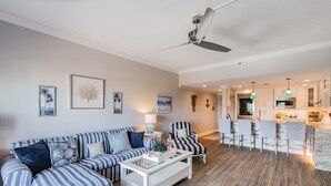 Ein Wohnzimmer mit gestreiften Sofas, einem Couchtisch und einer Küchenzeile mit Barhocker.