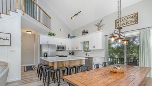 Une cuisine moderne avec des meubles blancs, un îlot central en bois et des tabourets de bar.