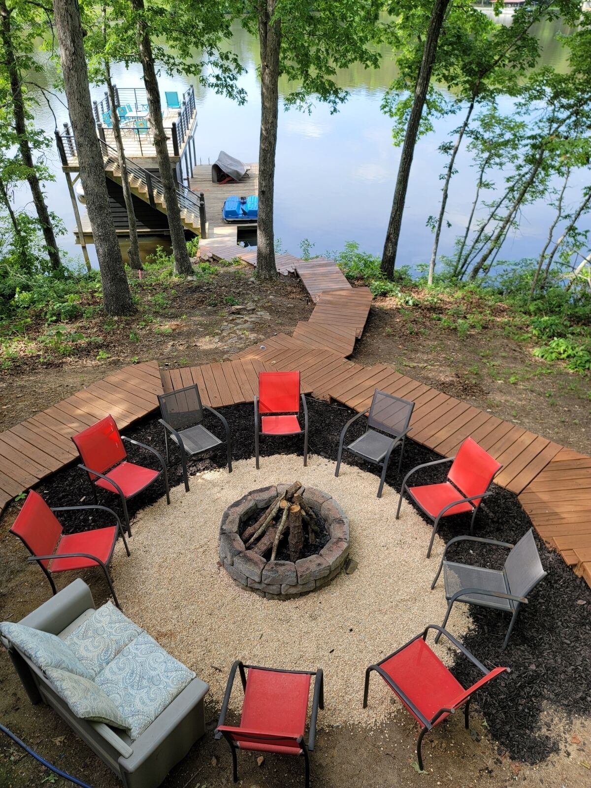 A circular outdoor seating area with a fire pit, surrounded by wooden decking and red and gray chairs.