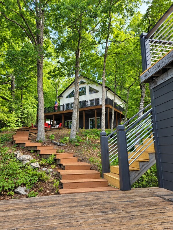 A two-story house with a deck, surrounded by trees.