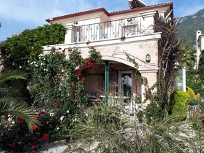 Ein zweistöckiges Gebäude mit Balkon, umgeben von üppiger Vegetation und blühenden Pflanzen.