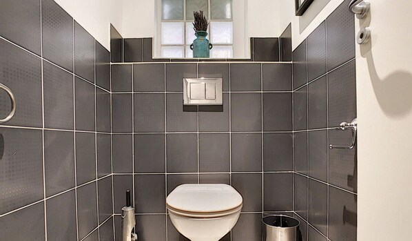 A modern bathroom with dark tiles, a toilet, a hand dryer, and a small window above the sink. - N&J - GLORY RIVIERA - Central - Close sea (Niza)