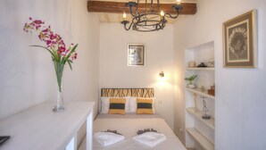 Un dormitorio con cama, una lámpara de araña, un jarrón con flores y una estantería con objetos decorativos.
