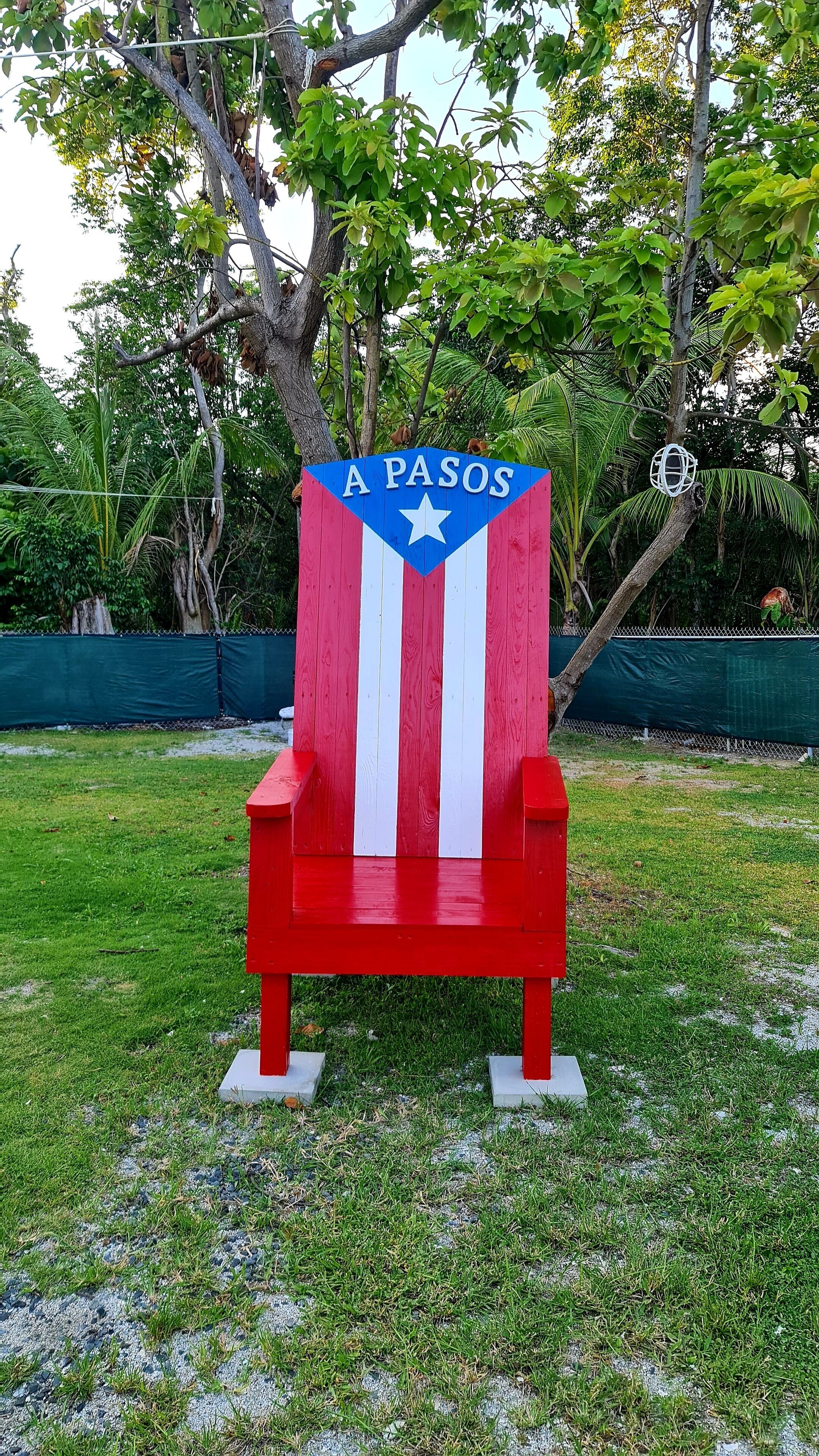 Une chaise à rayures rouges et blanches, sur laquelle est inscrit le mot « A PASOS », placée à l’extérieur, sur l’herbe.