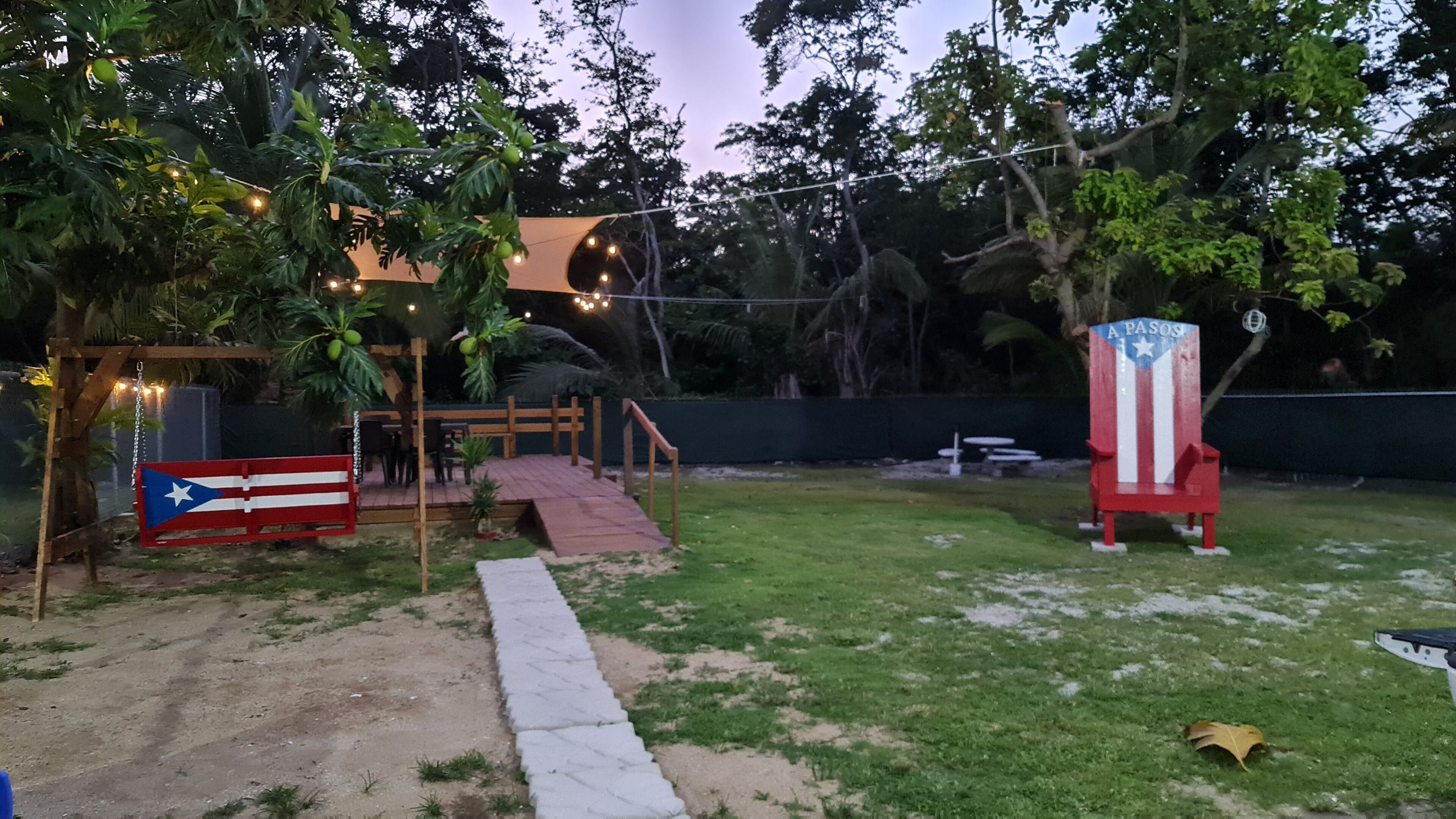 Un patio trasero con terraza, luces colgantes, una bandera y un asta de bandera.