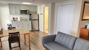 Un espacio habitable compacto con comedor, kitchenette, sofá gris y mesa de centro de madera.