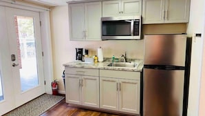 Una cocina con armarios de tonos claros, un refrigerador de acero inoxidable, un microondas y un lavamanos.