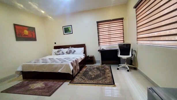Une chambre à coucher avec un lit, un bureau, une chaise, une fenêtre avec des stores, un tapis et un tableau au mur.