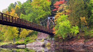 Eine Holzbrücke über einem ruhigen Fluss, umgeben von Herbstlaub.