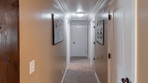 A hallway with beige walls, white trim, and a carpeted floor. There are framed pictures on the walls and a door with the number 66. - Classy, Clean & Comfortable - Close to Downtown (Kanab)