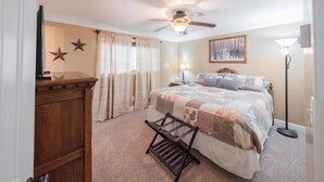 A bedroom with a bed, a ceiling fan, a nightstand, a lamp, and a wooden bench. - Classy, Clean & Comfortable - Close to Downtown (Kanab)