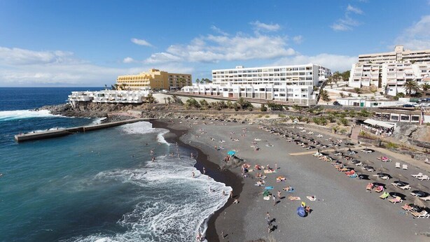 Un hotel frente al mar con varios pisos, una playa y un litoral rocoso.