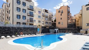 Una piscina rodeada de sillas de descanso y un muro de piedra.