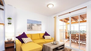 Un salón luminoso con un sofá amarillo, una mesa de centro de madera y un ventanal con vistas a un patio.