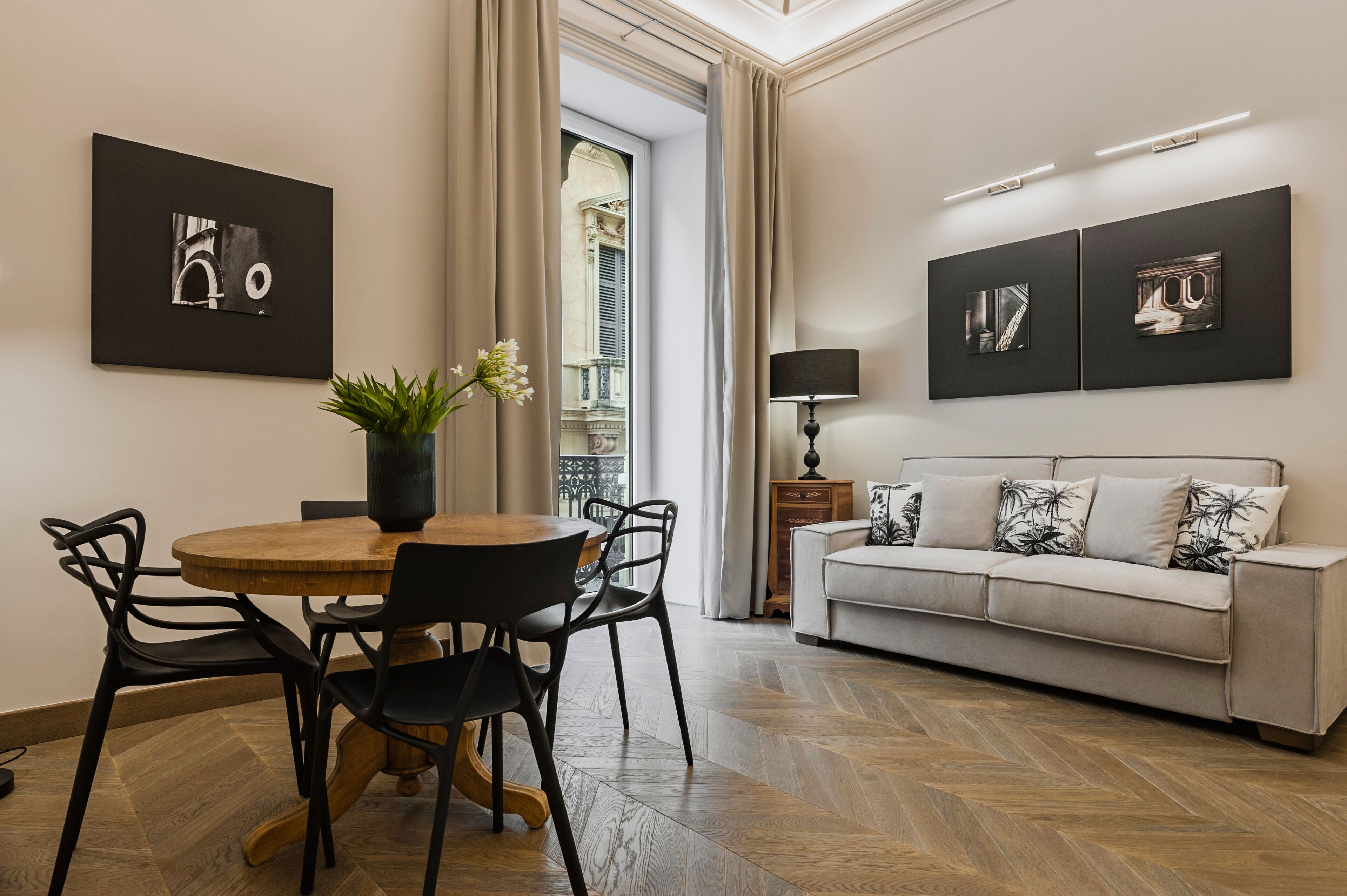 Un salon moderne avec une table ronde en bois, des chaises noires, un canapé beige agrémenté de coussins à motifs et des œuvres d’art accrochées aux murs.