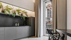 Una cocina moderna con armarios grises, encimera negra y suelo con estampado de espiga. Hay plantas en macetas sobre la encimera, y una zona de comedor con una mesa y sillas.