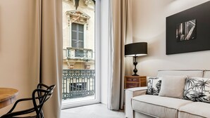 Una sala de estar moderna con un sofá, una mesa de comedor con sillas, una lámpara y vistas a un balcón con una reja de hierro forjado.