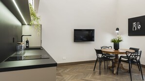 Una cocina moderna con estufa integrada, una mesa de comedor con sillas, un televisor montado en la pared y una planta colgante.