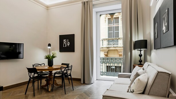 Una sala de estar moderna con comedor, un sofá, un televisor y un balcón con vista a un edificio.