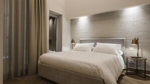 Una cama con ropa de cama blanca impecable, un cabecero de madera y dos lámparas de noche.