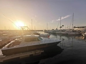 Un port de plaisance où sont amarrés de nombreux bateaux, un ciel dégagé et un soleil se couchant ou se levant.