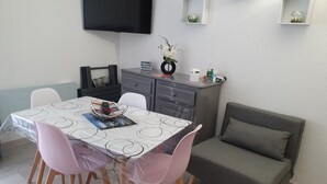 Un comedor con una mesa, sillas, un sofá, un televisor montado en la pared y un estante con objetos decorativos.