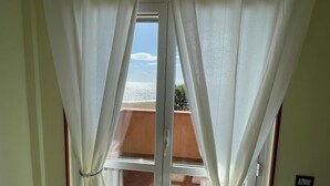 A window with white curtains, a view of the sea, and a balcony with a brown railing. - Apartment La Ginestra directly on the beach (Albinia)
