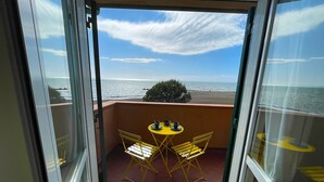 A balcony with a table and chairs, overlooking a beach with a clear sky. - Apartment La Ginestra directly on the beach (Albinia)