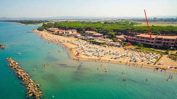 An aerial view of a coastal area with a beach, buildings, and a rocky shoreline. - Apartment La Ginestra directly on the beach (Albinia)