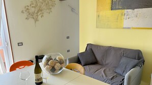 A room with a grey sofa, a white table with a wine bottle and glasses, and a decorative glass bowl. - Apartment La Ginestra directly on the beach (Albinia)