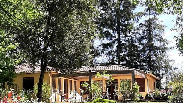 A building with a tiled roof, surrounded by lush greenery and trees. - Village of 10 lodgings with heated outdoor swimming pool, restaurant on 1 hectare (Calviac en Périgord)