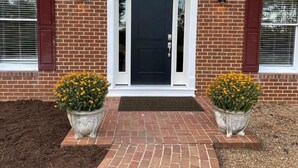 A brick house with a black front door, white trim, and two potted yellow flowers on either side.