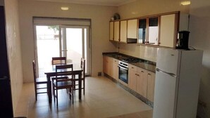 A kitchen with wooden cabinets, a gas stove, a refrigerator, and a dining area with chairs and a table. - Casa Do Castillo (Fisterra)