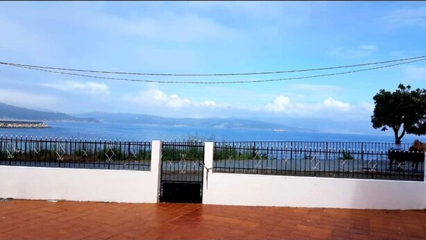 A coastal view with a metal fence and a gate, leading to a paved area. - Casa Do Castillo (Fisterra)