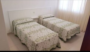 A room with two single beds, each with a floral-patterned bedspread, a white headboard, and a small shelf above the beds.